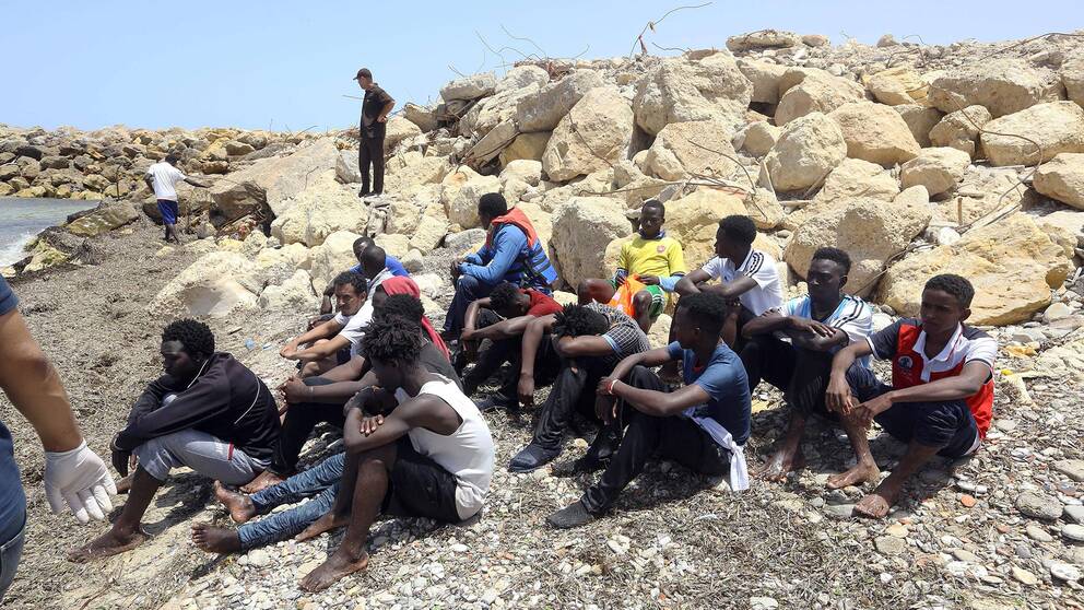 Migranter som räddades av den libyska kustbevakningen sitter på land öster om Tripoli.