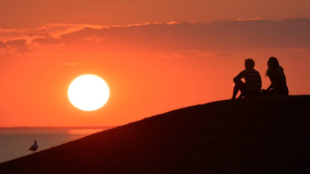 Två personer sitter vid en solnedgång.