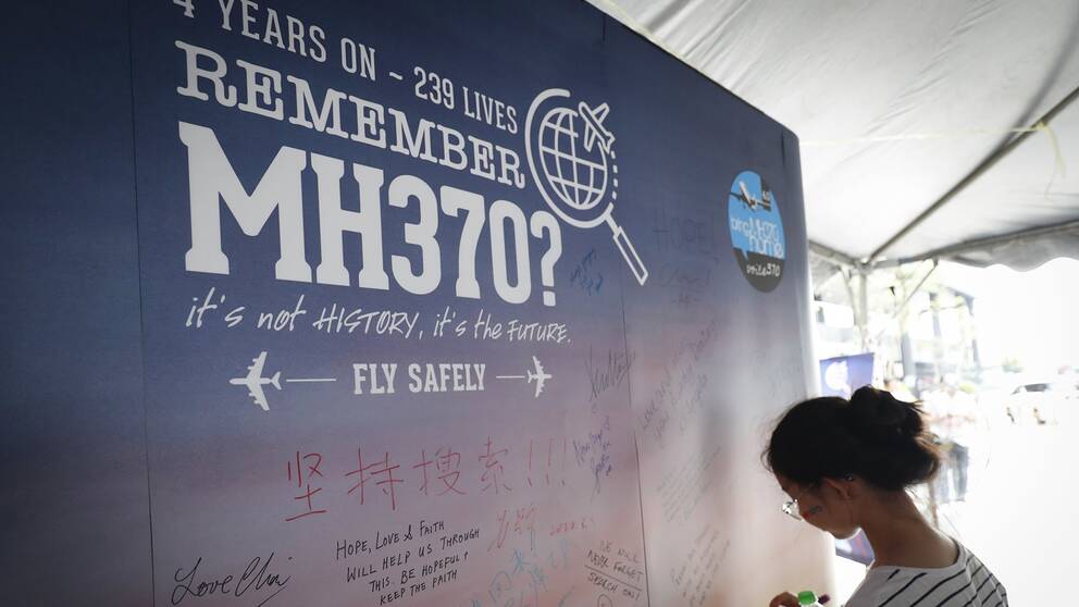 En ung tjej skriver ett kondoleansbudskap på en affisch som påminner om årsdagen av dagen då planet MH370 försvann.