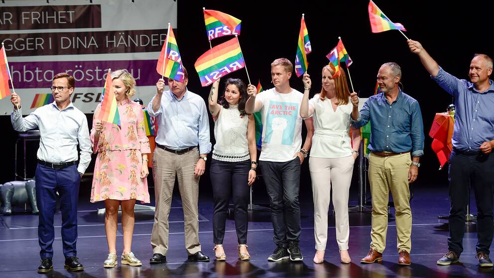 Åtta partiledare och språkrör höjer regnbågsflaggan på Kulturhusets scen under partiledardebatten.