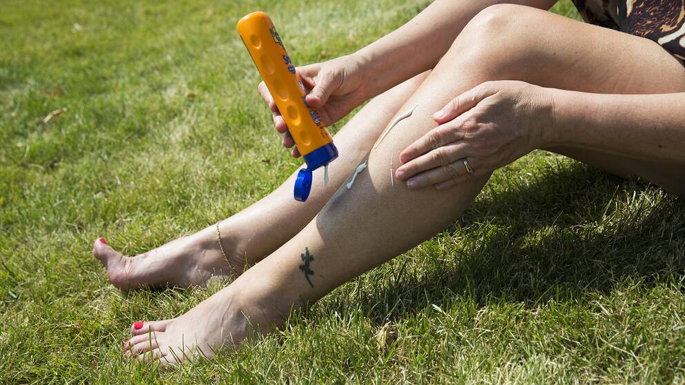 En kvinna sitter i gräset och smörjer in sina ben med solskydd.