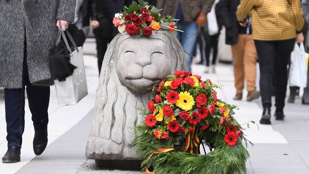 Blommor på ett betonglejon på drottninggatan i Stockholm.