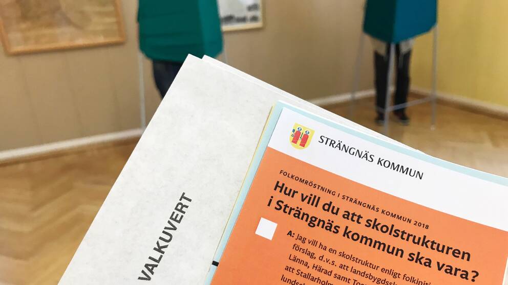Valsedel och  valkuvert, i bakgrunden syns två röstskynken i vallokalen i Härad i Strängnäs