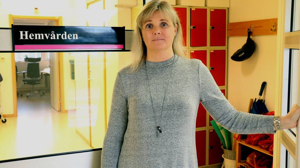 Enhetschefen Maria Möller står vid en dörr med en skylt där det står hemvården på. 