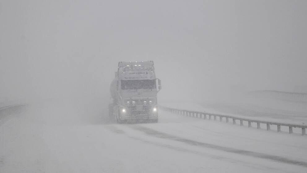 Vit lastbil kör i snöstorm.