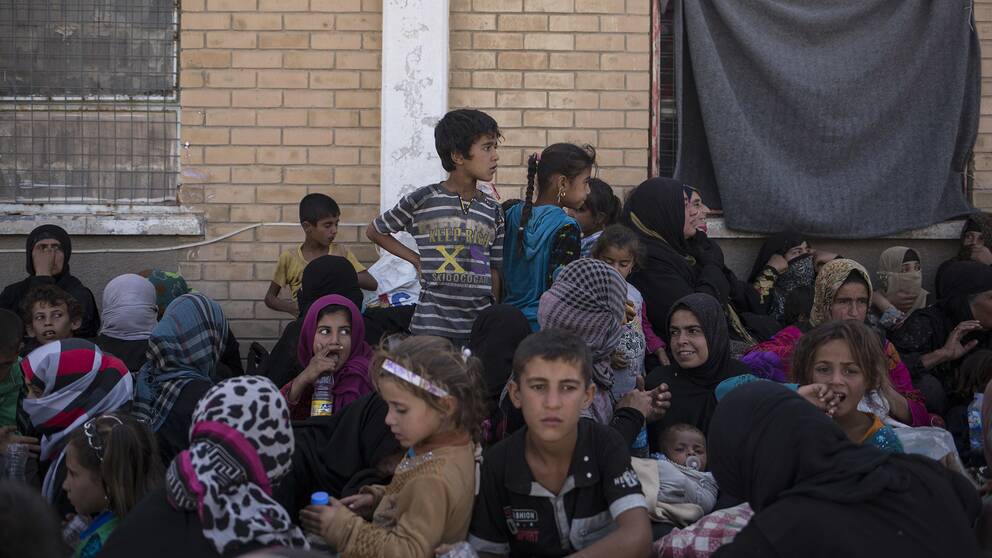 Barn i olika åldrar sitter utanför en byggnad i Irak.