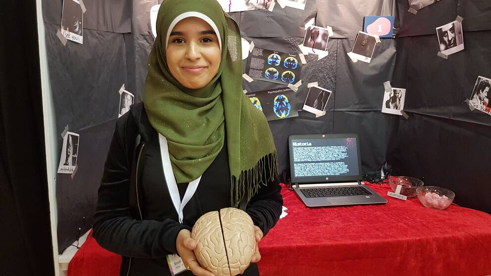 En ung tjej står vid sin monter och håller i en modell av en hjärna. 