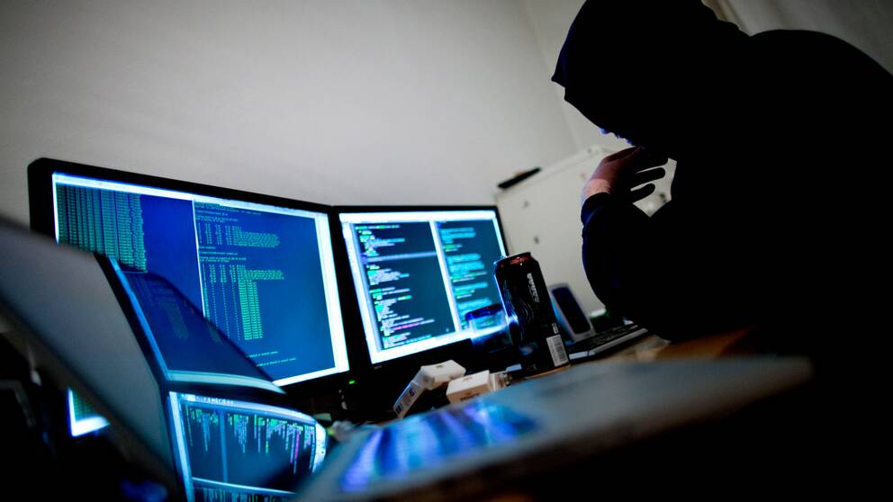 En person som sitter vid en dator, flera skärmar med koder på