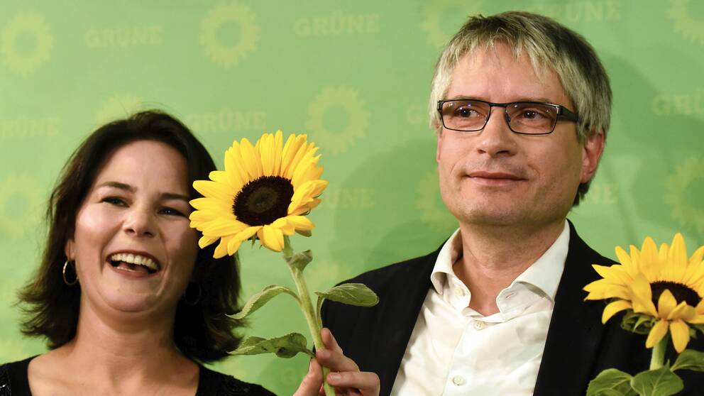 Anna Baerbock och Sven Giegold är fglada och håller upp solrosor.