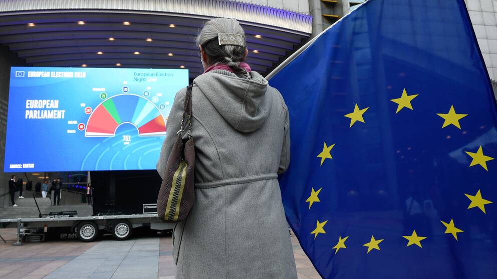 En kvinna står med en EU-flagga utanför Europaparlamentet.