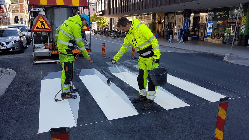 Två män målar om övergångsstället vid Näbbtorget i Örebro så att det får en tredimitionell effekt.