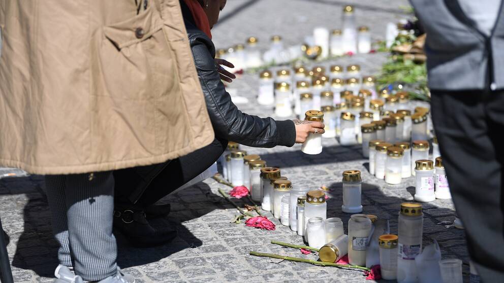 En person tänder ljus vid en minnesplats för de tre personer som dödats i skjutningar i Sätra i Stockholm.