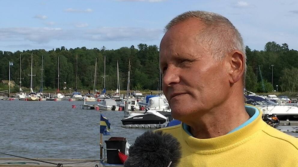 Carl Hamilton står framför en hamn med båtar.