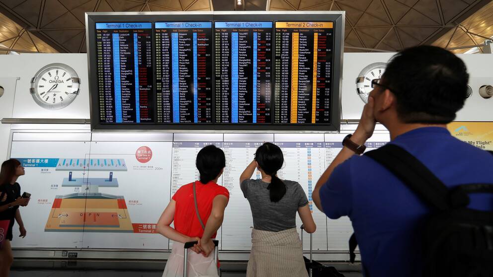 Passagerare kollar på avgångstavlan på Hongkongs flygplats.
