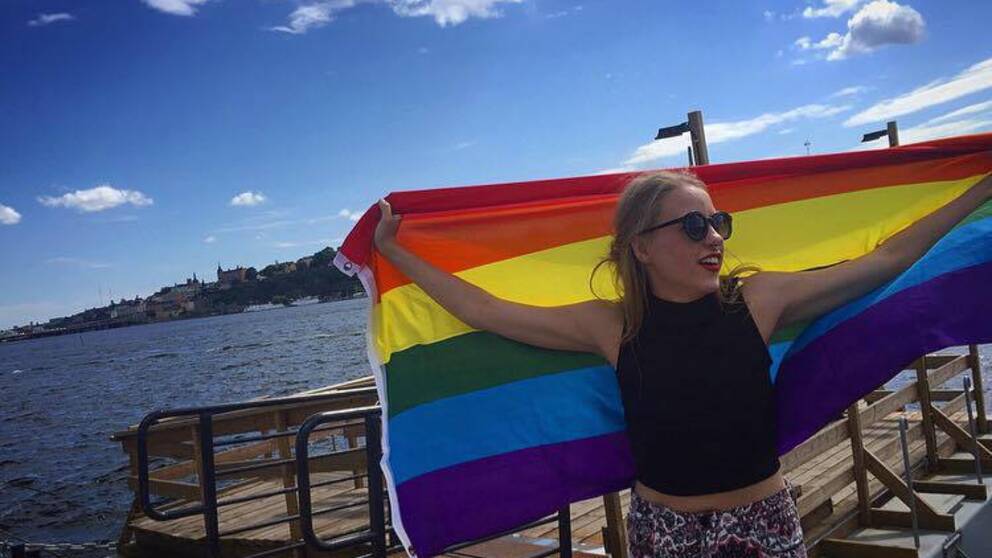 Johanna Sköld på en brygga där hon håller upp en regnbågsflagga.