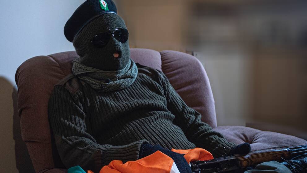 En maskerad man från terrorgruppen CIRA sitter i en fåtölj med ett vapen i famnen.