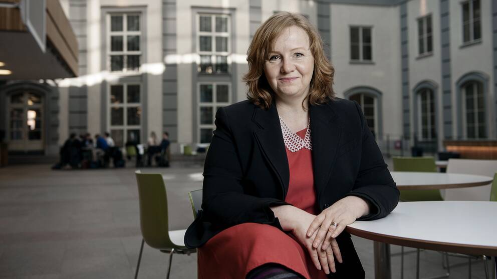 Lena Lid Falkman sitter klädd i röd klänning vid ett bord och tittar mot kameran.