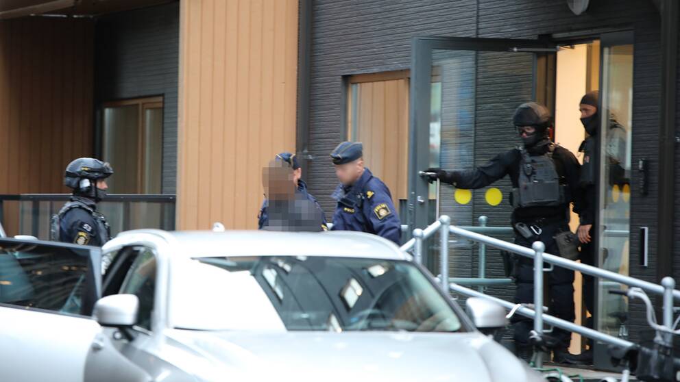 flera polismän i uniform och maskerade poliser för ut en person som 