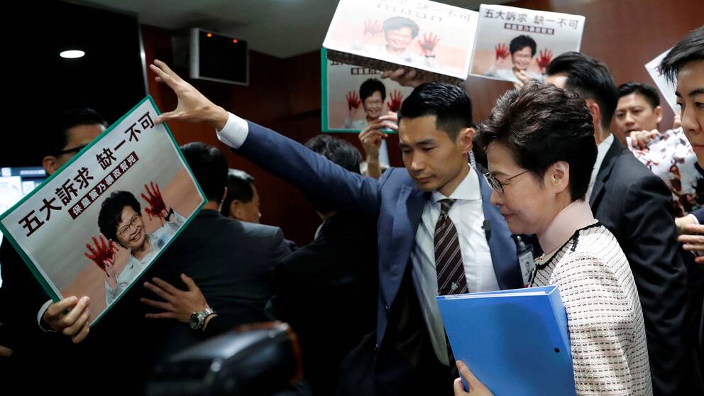 Carrie Lam eskorteras ut av säkerhetsvakter.