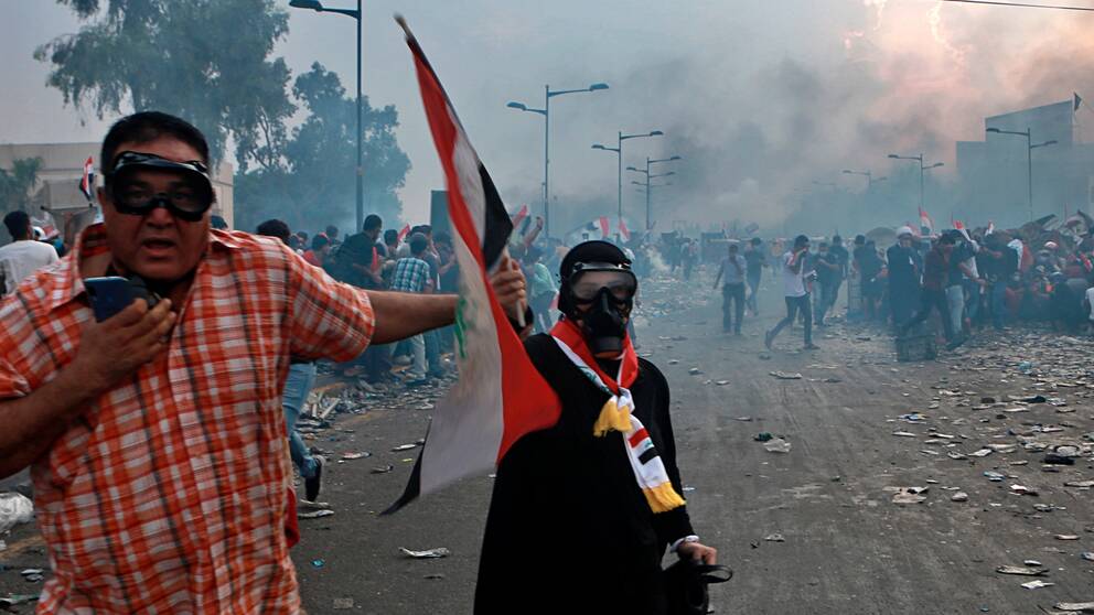Demonstranter som tar skydd när säkerhetsstyrkor skjuter tårgas mot dem i Bagdad under måndagen.