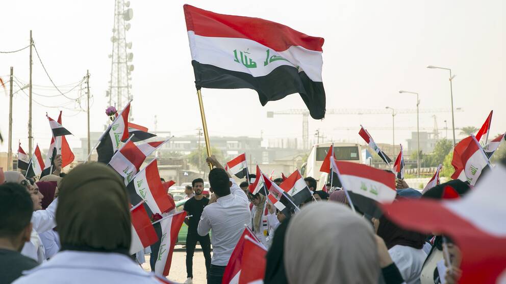 Demonstranter i Irak håller upp den irakiska flaggan.