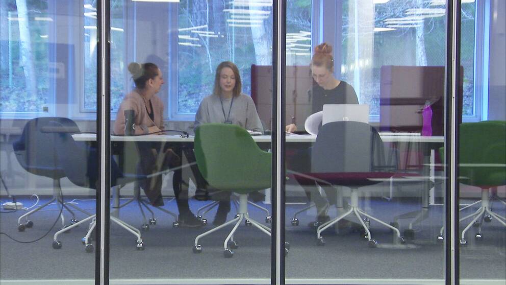 Tre kvinnor sitter vid ett konferensbord. Syns genom glasvägg.
