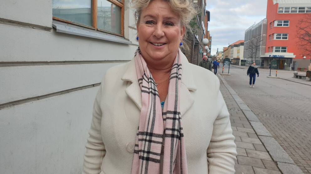 Anette står på en gata i Linköping, klädd i ljus kappa.