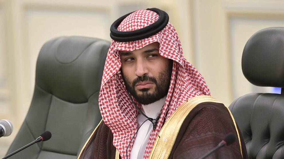 En bild på saudiske kronprinsen i traditionell saudisk klädsel sittandes i ett stol vid ett konferensbord.