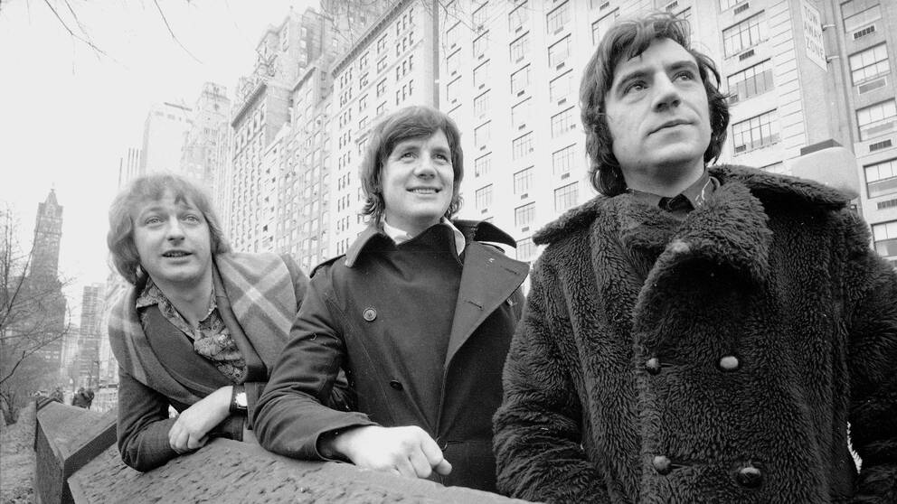 Svartvitt foto på Graham Chapman, Michael Palin och Terry Jones som står i en stadsmiljö.