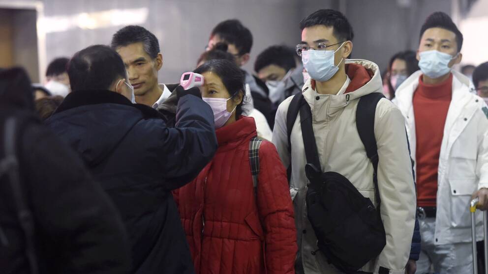 Personal använder termometer för att kontrollera temperaturen på passagerare som anländer från Wuhan på en tågstation i Hangzhou.