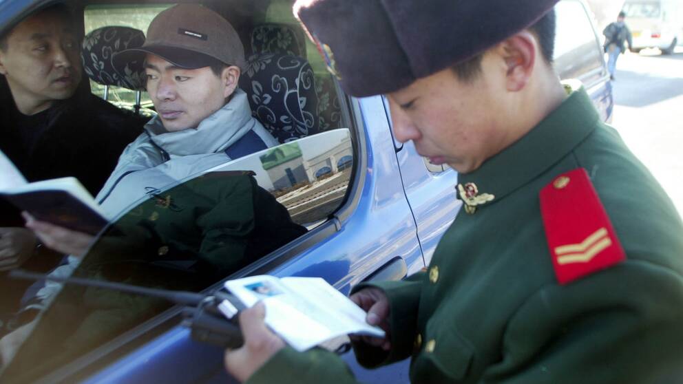 En kinesisk gränspolis kollar passen för två personer i en bil vid gränsen mellan Kina och Ryssland