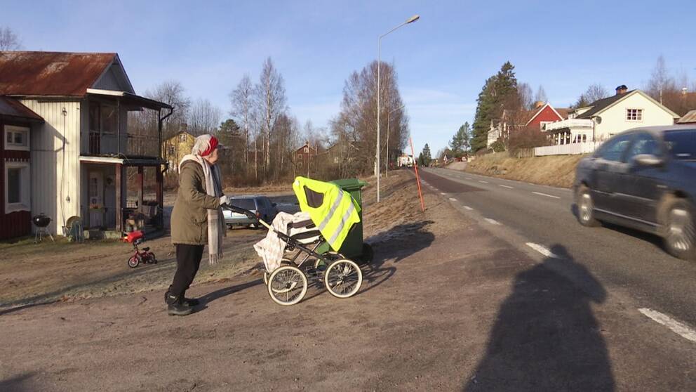 Kvinna försöker ta sig över en väg med barnvagn, bil kör förbi.