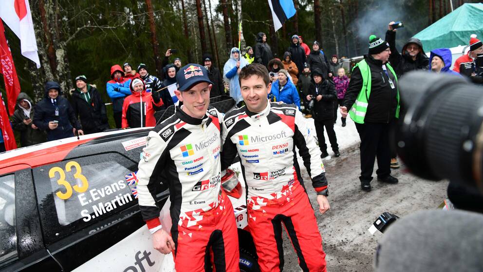 Elfyn Evans och Scott Martin poserar för bilder samtidigt som publik syns i bakgrunden.
