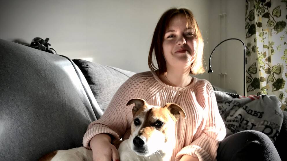 Amanda Wall i rosa tröja sitter i en grå soffa med en liten brunvit hund.