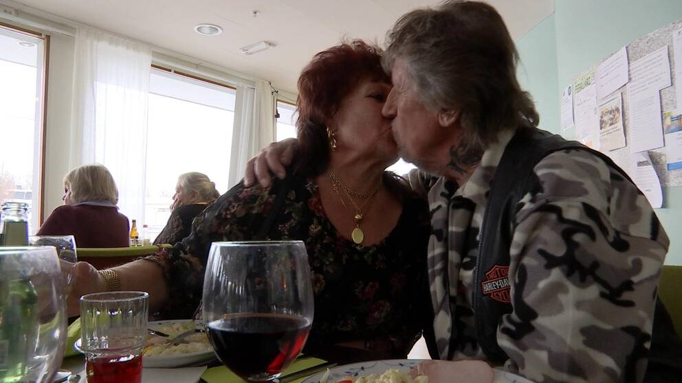 En kvinna och en man pussas med vinglas i förgrunden.