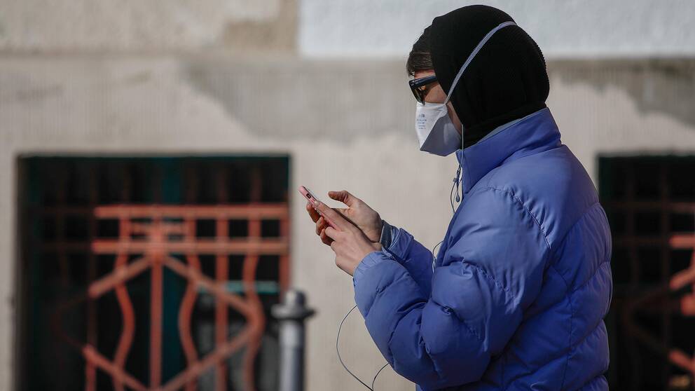 En person med mask kollar i mobilen. 