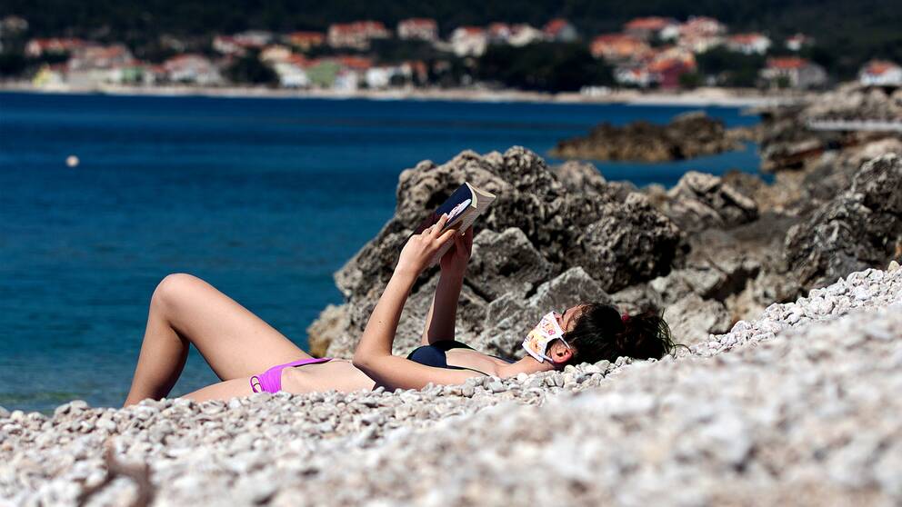 En ensam kvinna i munskydd som solbadar på en strand på Cres i Kroatien. Tidigare år har stranden varit full med människor den här tiden på året.