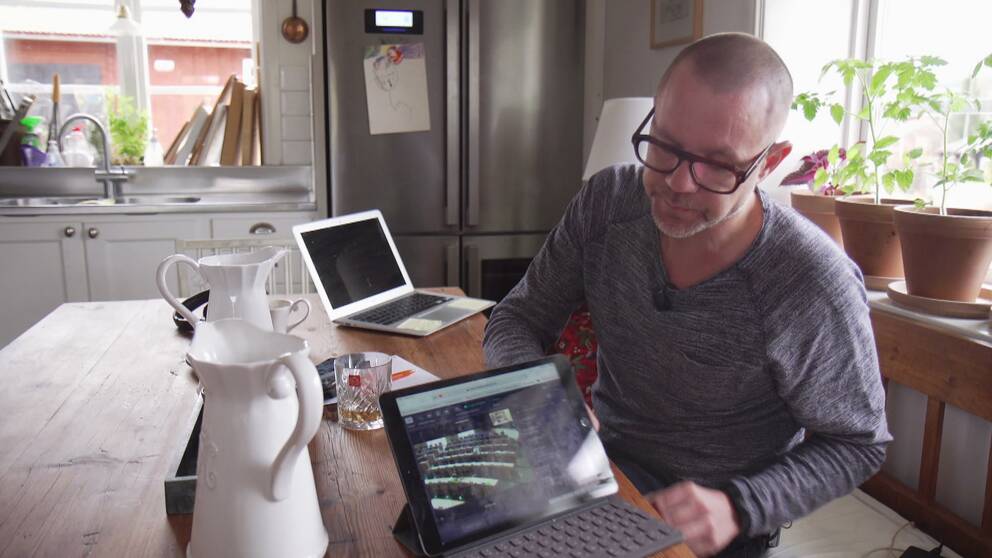en man sitter vid köksbord med laptop, bild från EU-parlamentet syns på skärmen
