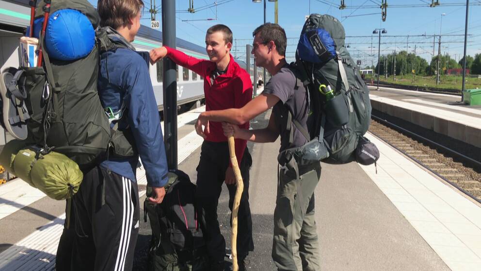 tre killar med ryggsäck utanför tåg på perrong