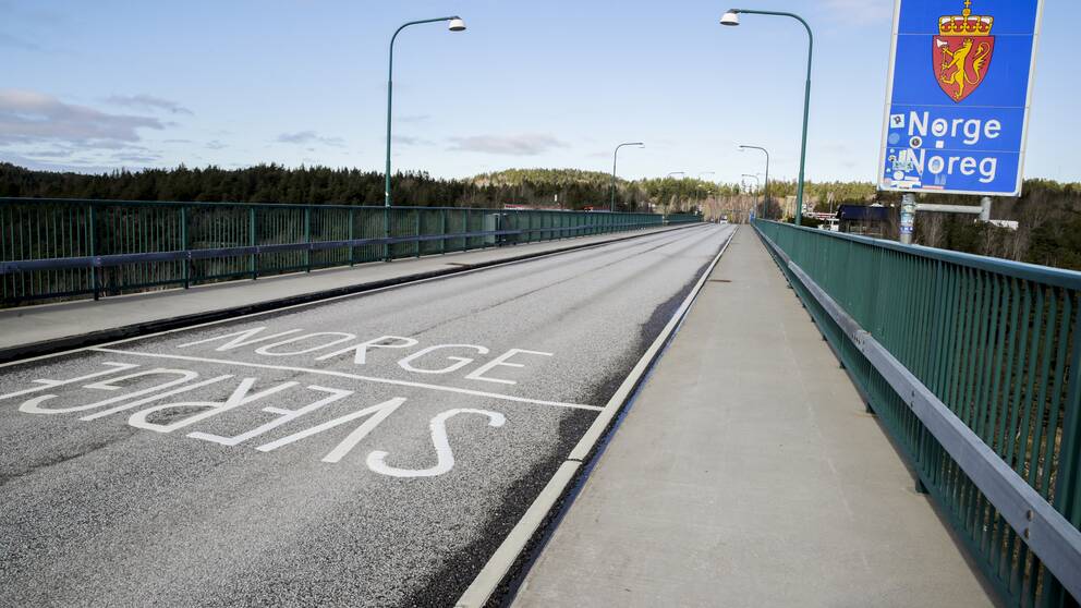 En asfalterad väg med orden Sverige och Norge skrivet i vit färg. Vid sidan om en blå skylt med texten ”Norge” i vitt.