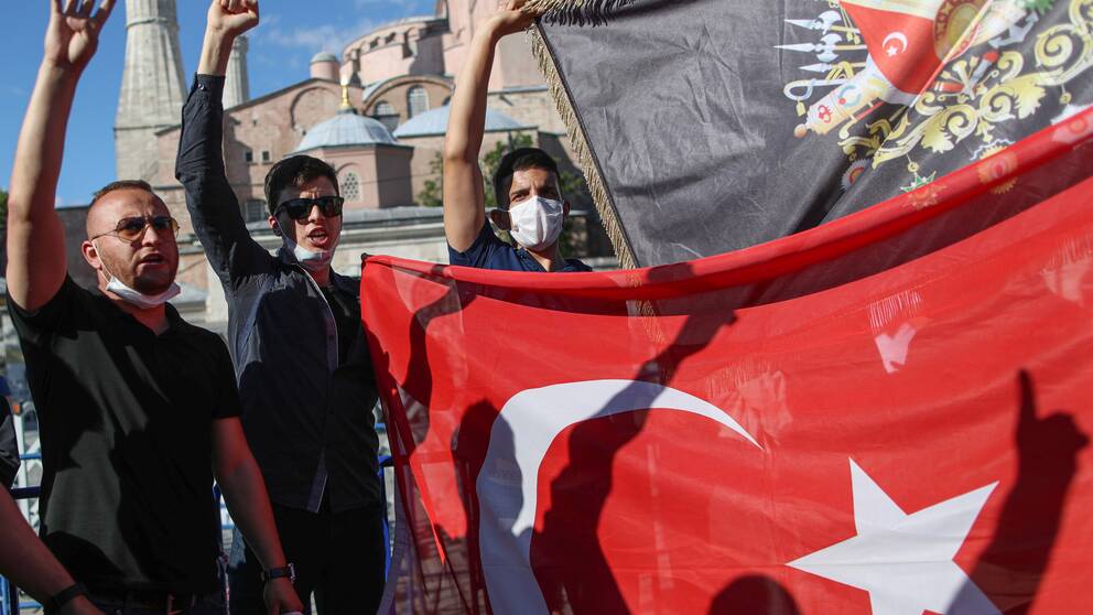 Personer håller upp turkiska och ottomanska flaggor framför Hagia Sofia i Istanbul, Turkiet efter dombeslutet att muséet kan bli moské.