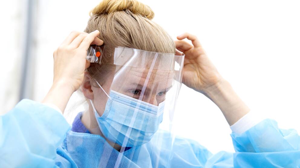 kvinna i blå sjukhusklädsel med uppsatt hår justerar skyddsvisir