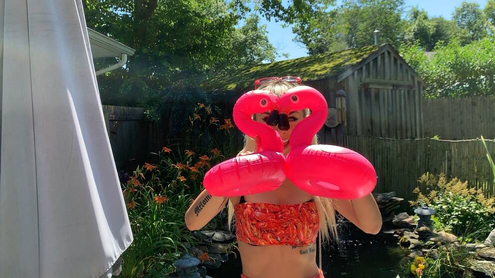 Artisten Jasmine Kara står i bikini och håller upp två rosa plastflamingos, som bildar ett hjärta, framför ansiktet.
