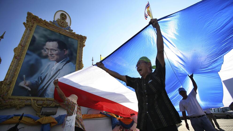 En supporter till regimen viftar med en flagga framför ett porträtt av den thailändska kungen Bhumibol Adulyadej.