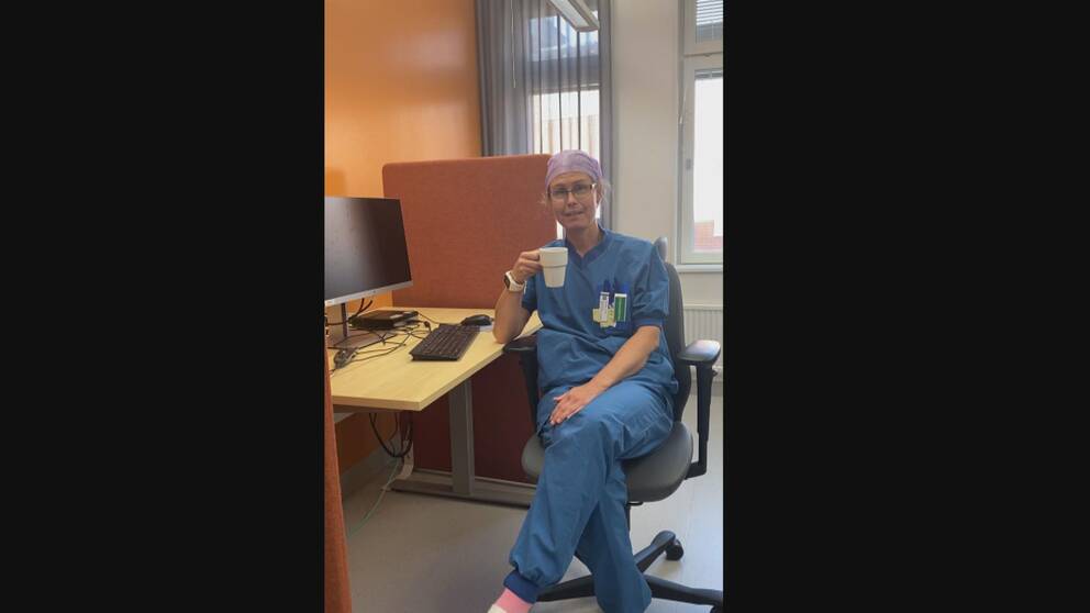 Therése sitter i arbetskläder i ett datarum på sjukhuset med en kaffekopp i handen och ler snett.