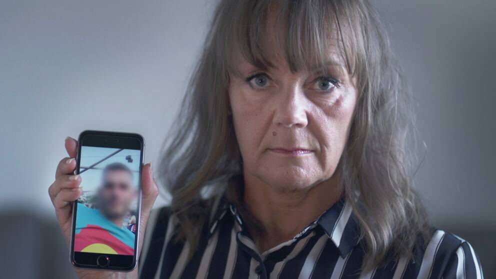 Lena håller upp en mobil med bild på en man som en nätbedragare använt för att lura henne på pengar.