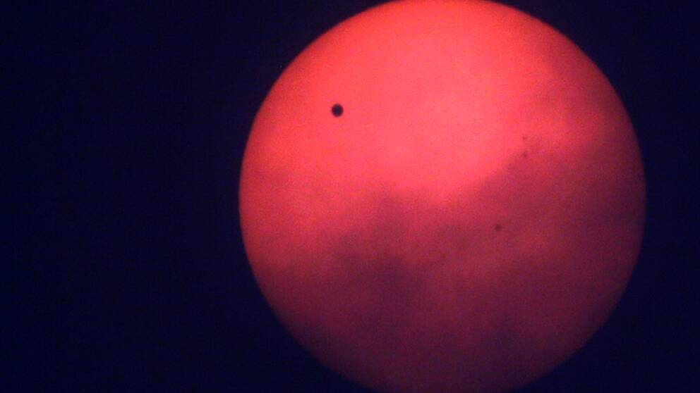 En bild på planeten Venus som lyser rött ute i den mörka rymden.