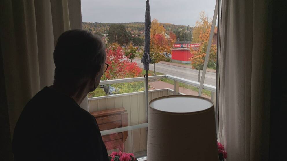 en äldre dam står med ryggen mot kameran och tittar ut mot en väg i Rättvik