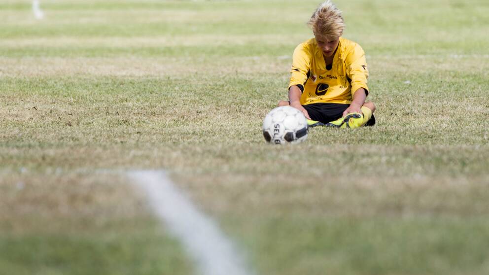 En ung ensam fotbollsspelare sitter på gräsmattan och deppar