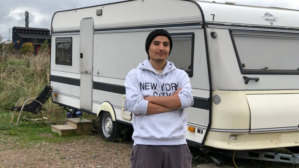 Salman  Yosofi står framför den vita husvagn han bor i utanför Staffanstorp.